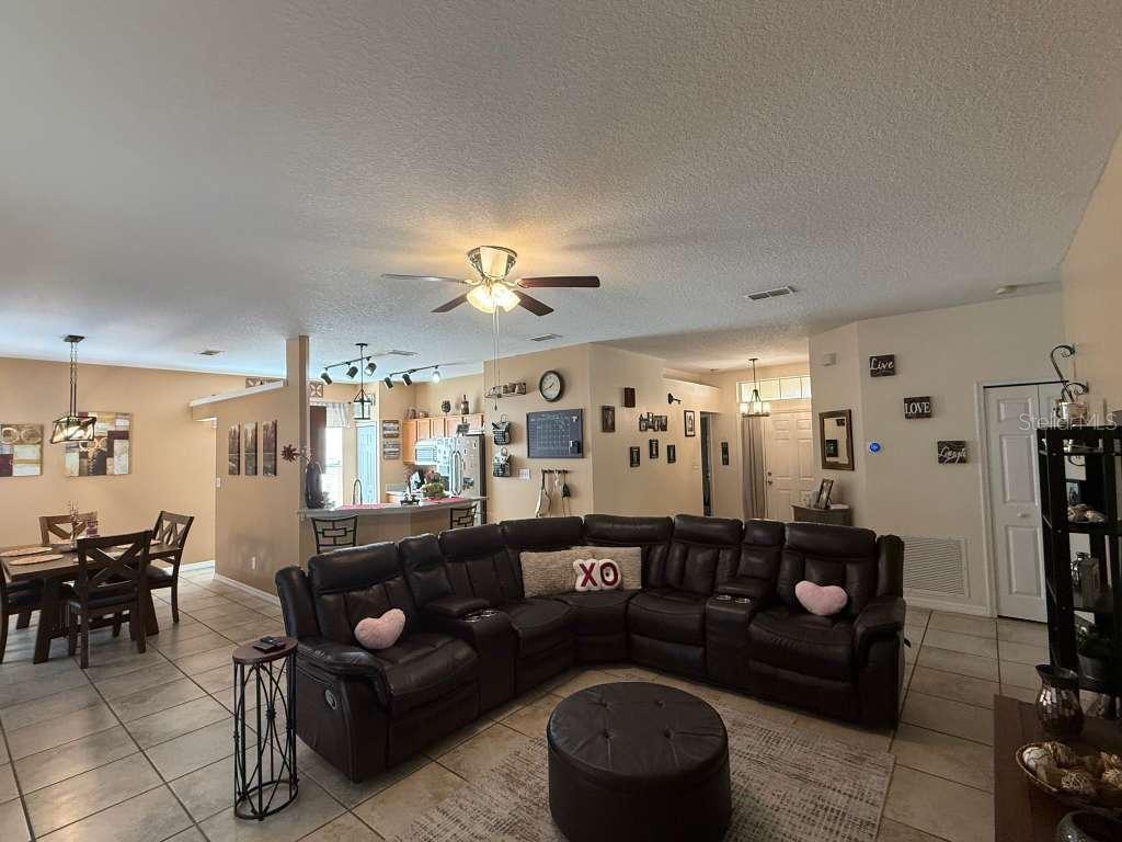 A living room with a large brown sectional sofa, tile flooring, and an open kitchen — 1166 DEKLEVA DRIVE, APOPKA, FL