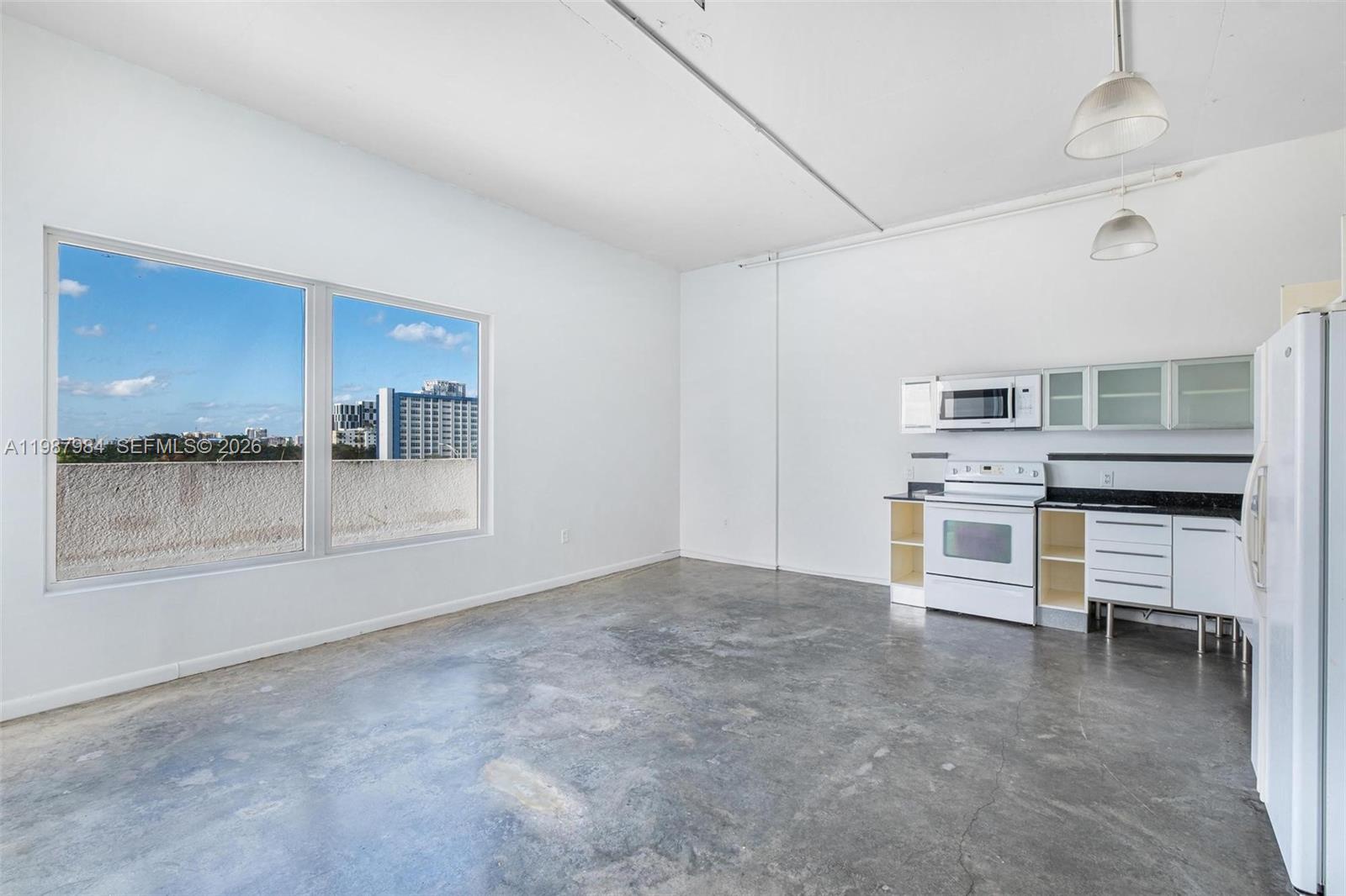 An unfurnished room features a small kitchenette, concrete floors, and a large window — 10 SW South River Dr # 609, Miami FL 33130, MIAMI, FL