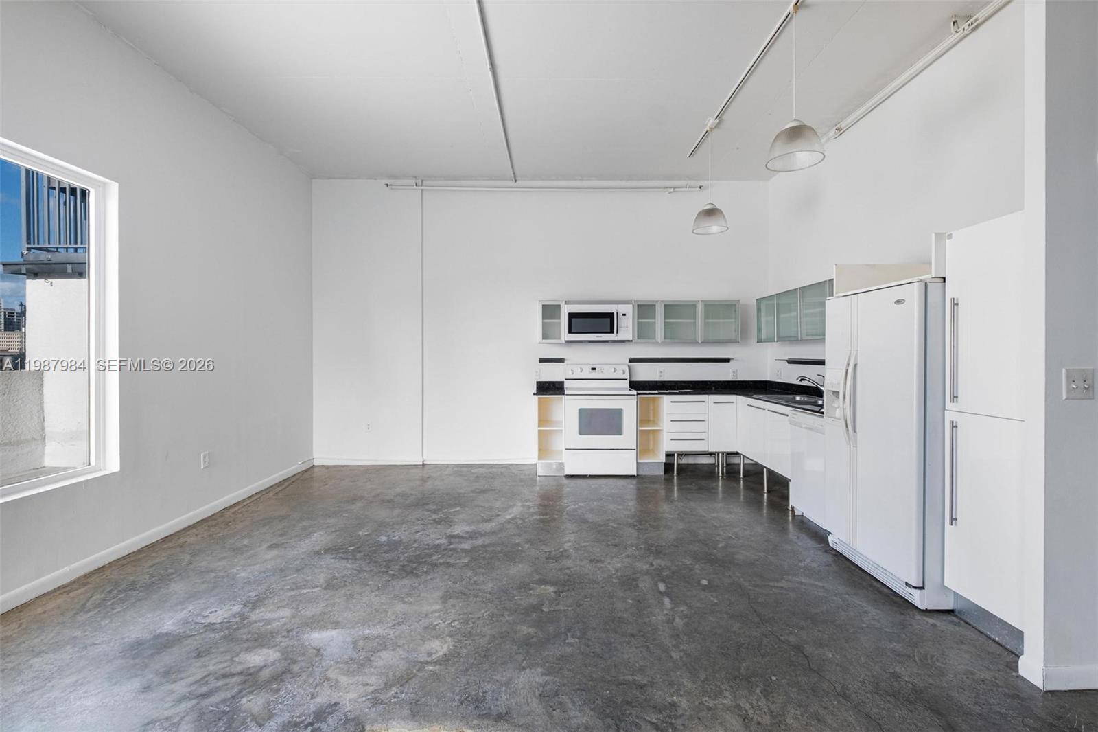 A kitchen with white appliances and cabinets sits in an open room with concrete floors — 10 SW South River Dr # 609, Miami FL 33130, MIAMI, FL