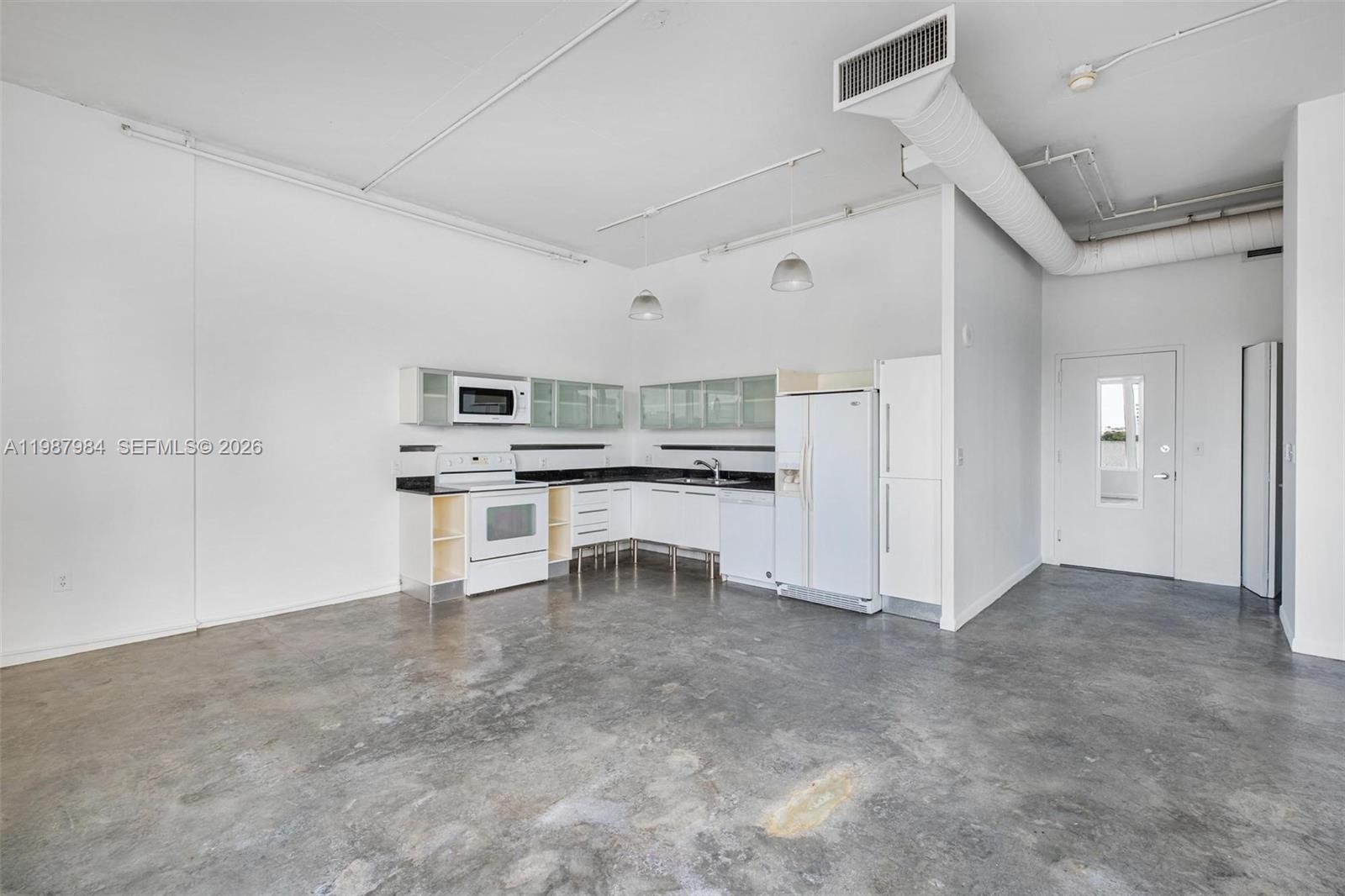 An open-concept kitchen features white cabinetry, white appliances, and exposed concrete flooring — 10 SW South River Dr # 609, Miami FL 33130, MIAMI, FL