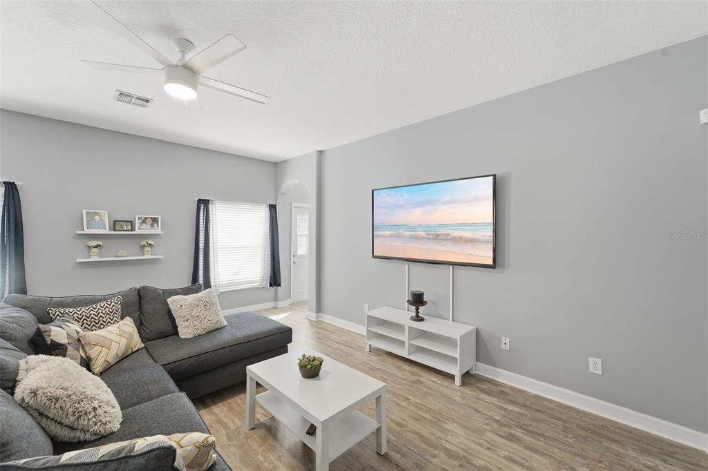 A living room features a grey sectional sofa, a white coffee table, and a wall-mounted television — 18124 SAXONY LANE, ORLANDO, FL