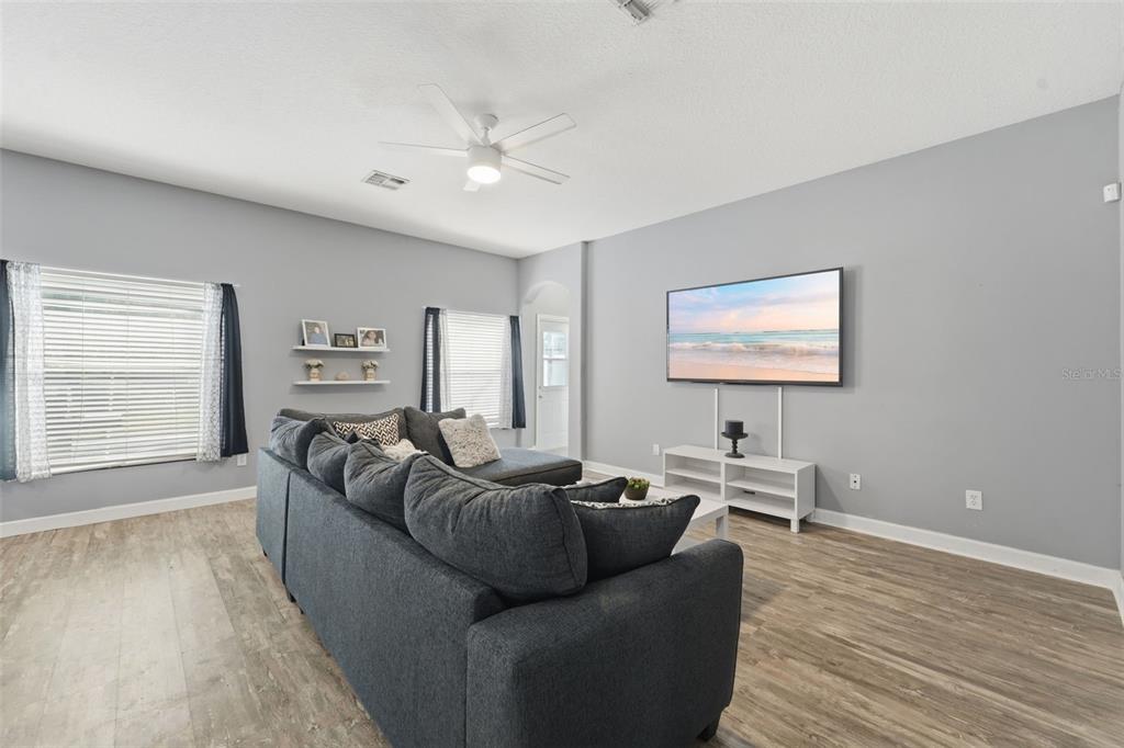 A living room features gray walls, wood-look flooring, a large sectional sofa, and a wall-mounted television — 18124 SAXONY LANE, ORLANDO, FL