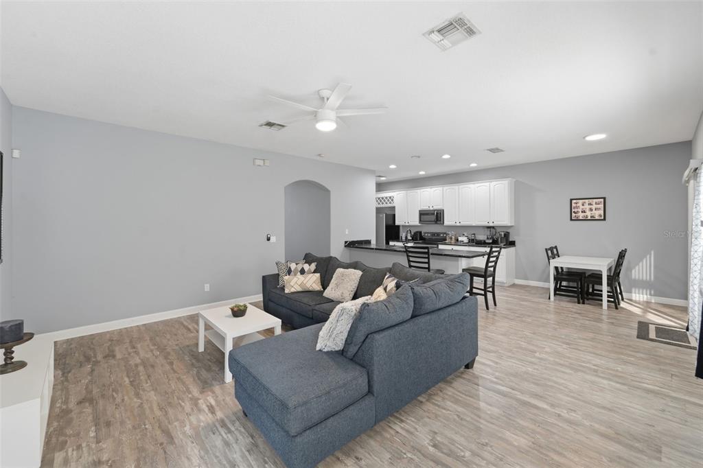 An open-concept living room and kitchen featuring gray walls, wood-look flooring, and a sectional sofa — 18124 SAXONY LANE, ORLANDO, FL