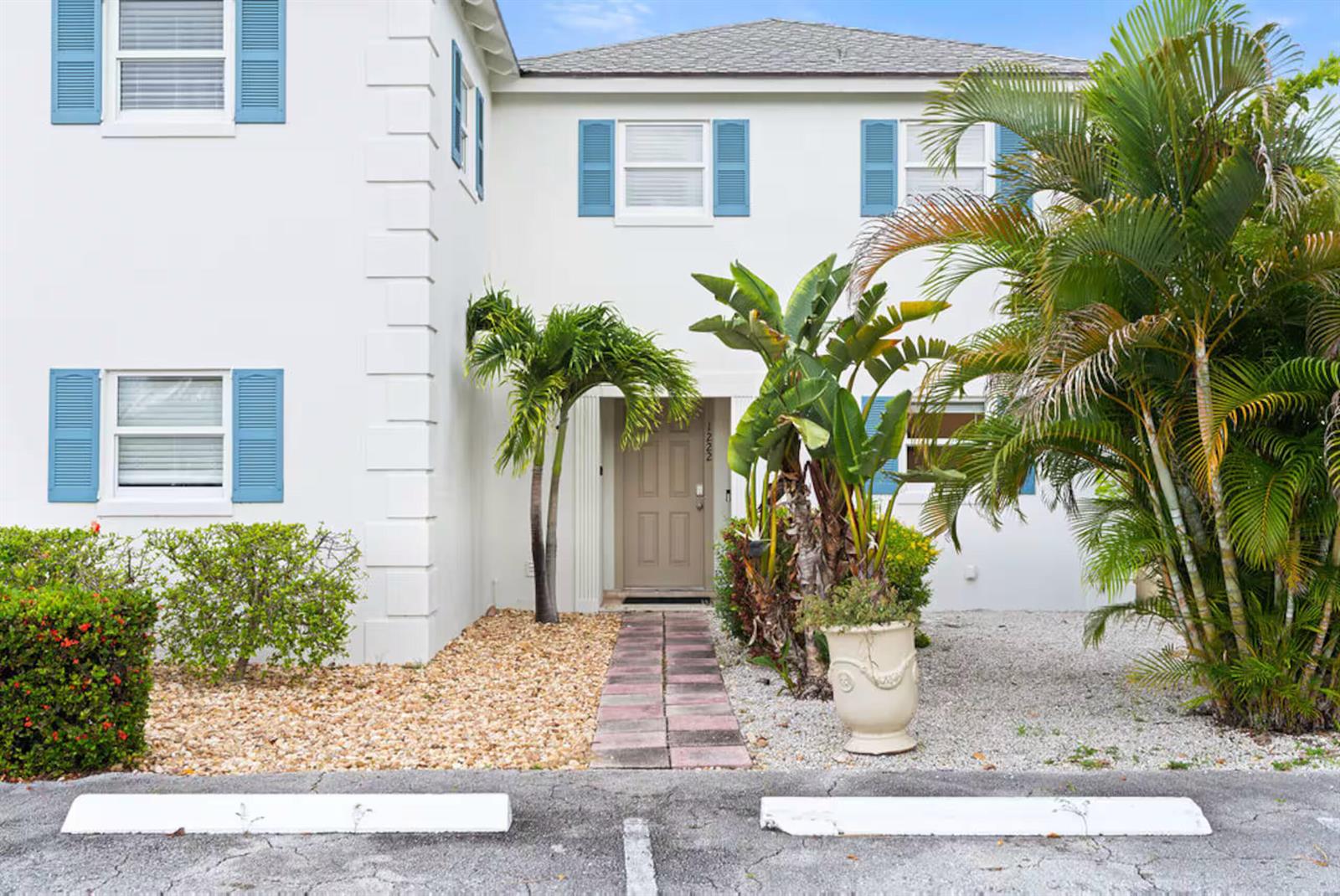 A two-story white building features blue shutters, a brown front door, and tropical landscaping — 1216 Surf Road, Singer Island FL 33404, SINGER ISLAND, FL
