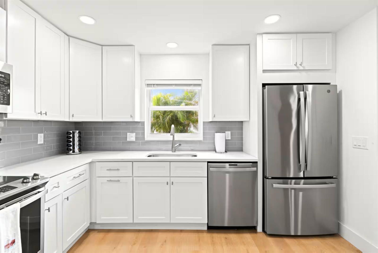 A kitchen with white cabinets, stainless steel appliances, gray subway tile backsplash, and wood flooring — 1216 Surf Road, Singer Island FL 33404, SINGER ISLAND, FL