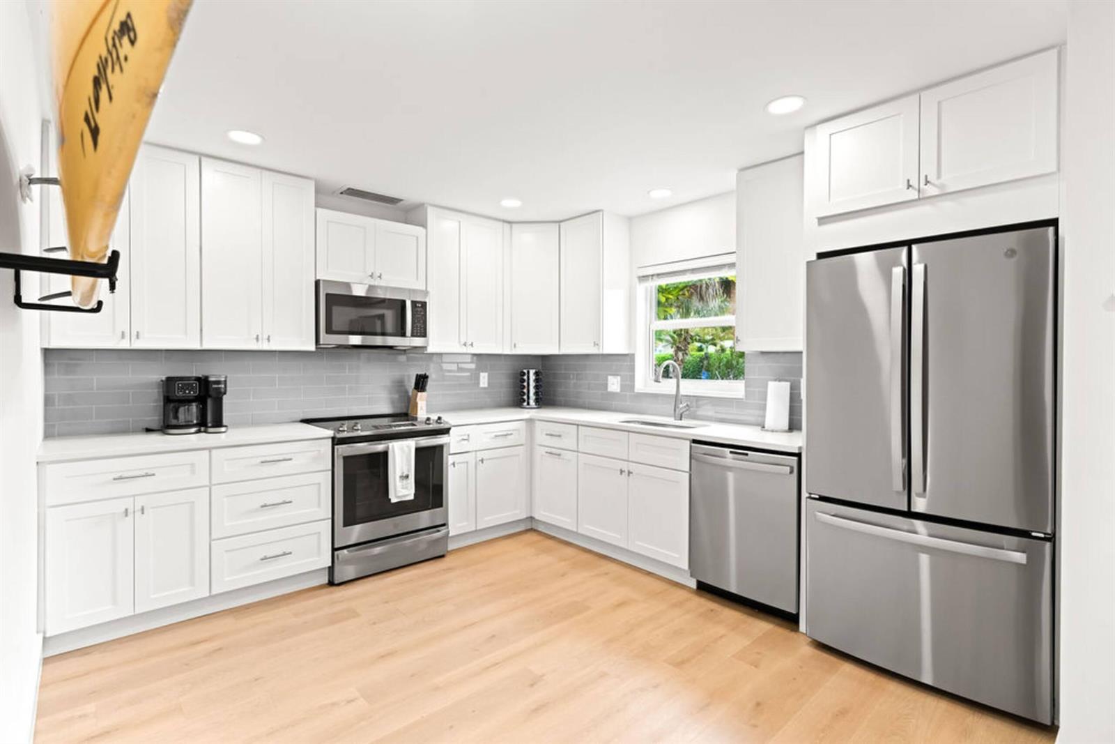 A modern kitchen features white cabinetry, stainless steel appliances, gray subway tile, and light wood flooring — 1216 Surf Road, Singer Island FL 33404, SINGER ISLAND, FL