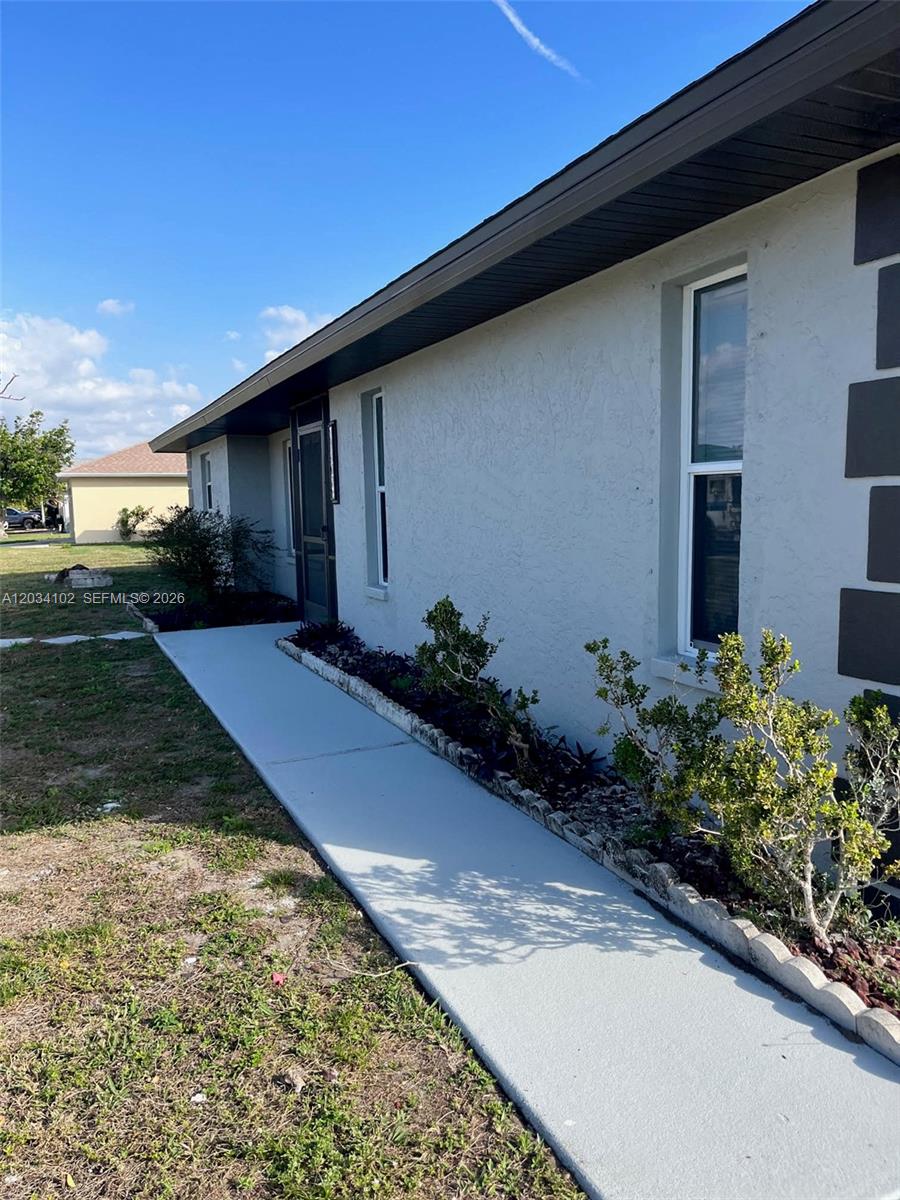 A concrete walkway leads along the side of a light-colored stucco house with windows — 1402 SE 34th ST # 0, Cape Coral FL 33904, CAPE CORAL, FL