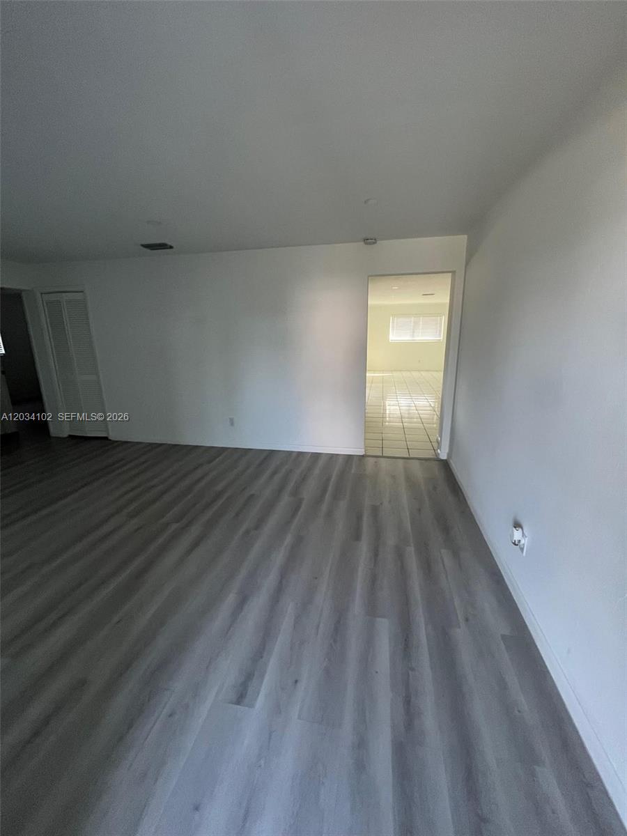 A room with gray wood-look flooring leads through a doorway into a tiled space — 1402 SE 34th ST # 0, Cape Coral FL 33904, CAPE CORAL, FL