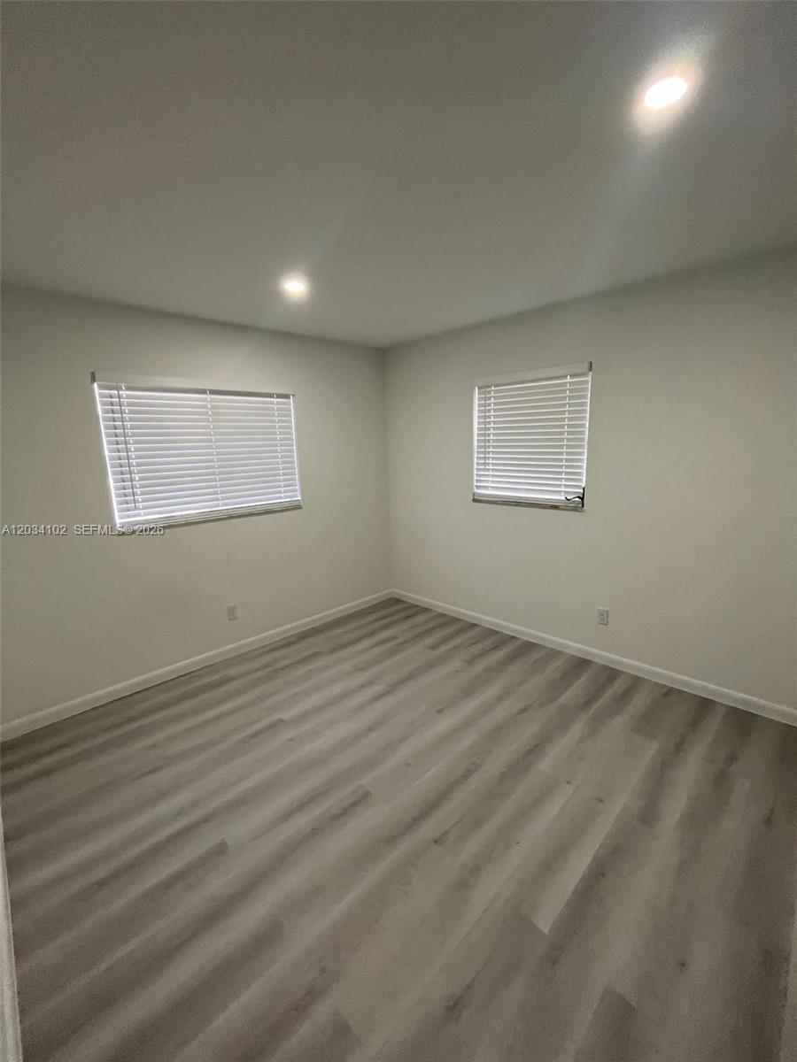 An empty room features light-colored wood-look flooring, white walls, and two windows with blinds — 1402 SE 34th ST # 0, Cape Coral FL 33904, CAPE CORAL, FL