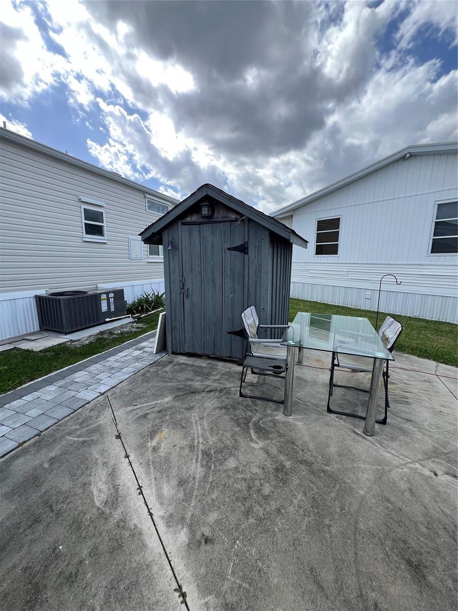 A gray wooden shed sits on a concrete patio between two white mobile homes — 5355 SE 64th Terrace, Okeechobee FL 34974, OKEECHOBEE, FL