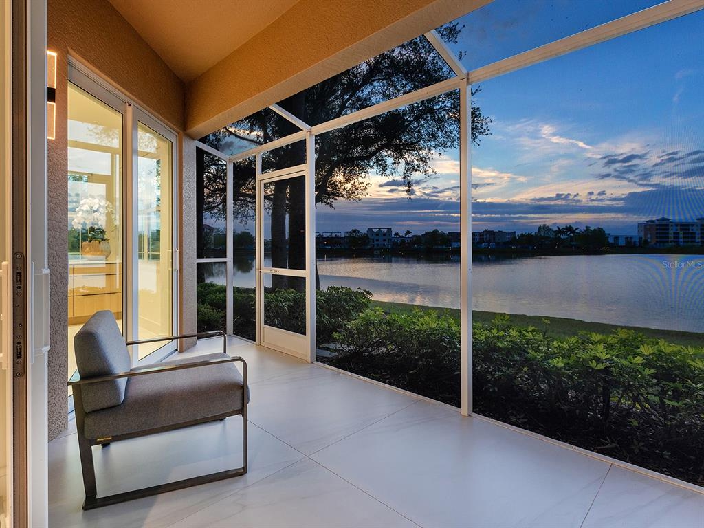 A screened-in patio with tile flooring overlooks a lake at sunset — 6427 MOORINGS POINT CIRCLE UNIT 101, LAKEWOOD RANCH, FL