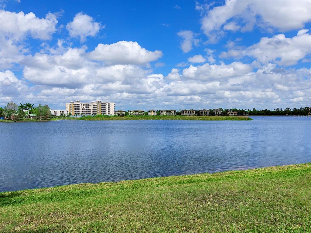 A view of a lake with a grassy foreground and buildings in the distance — 6427 MOORINGS POINT CIRCLE UNIT 101, LAKEWOOD RANCH, FL