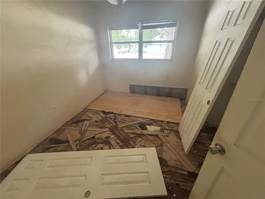 A bedroom with a damaged floor, exposed subflooring, and a detached door on the floor — 5620 2ND AVENUE DRIVE W, BRADENTON, FL