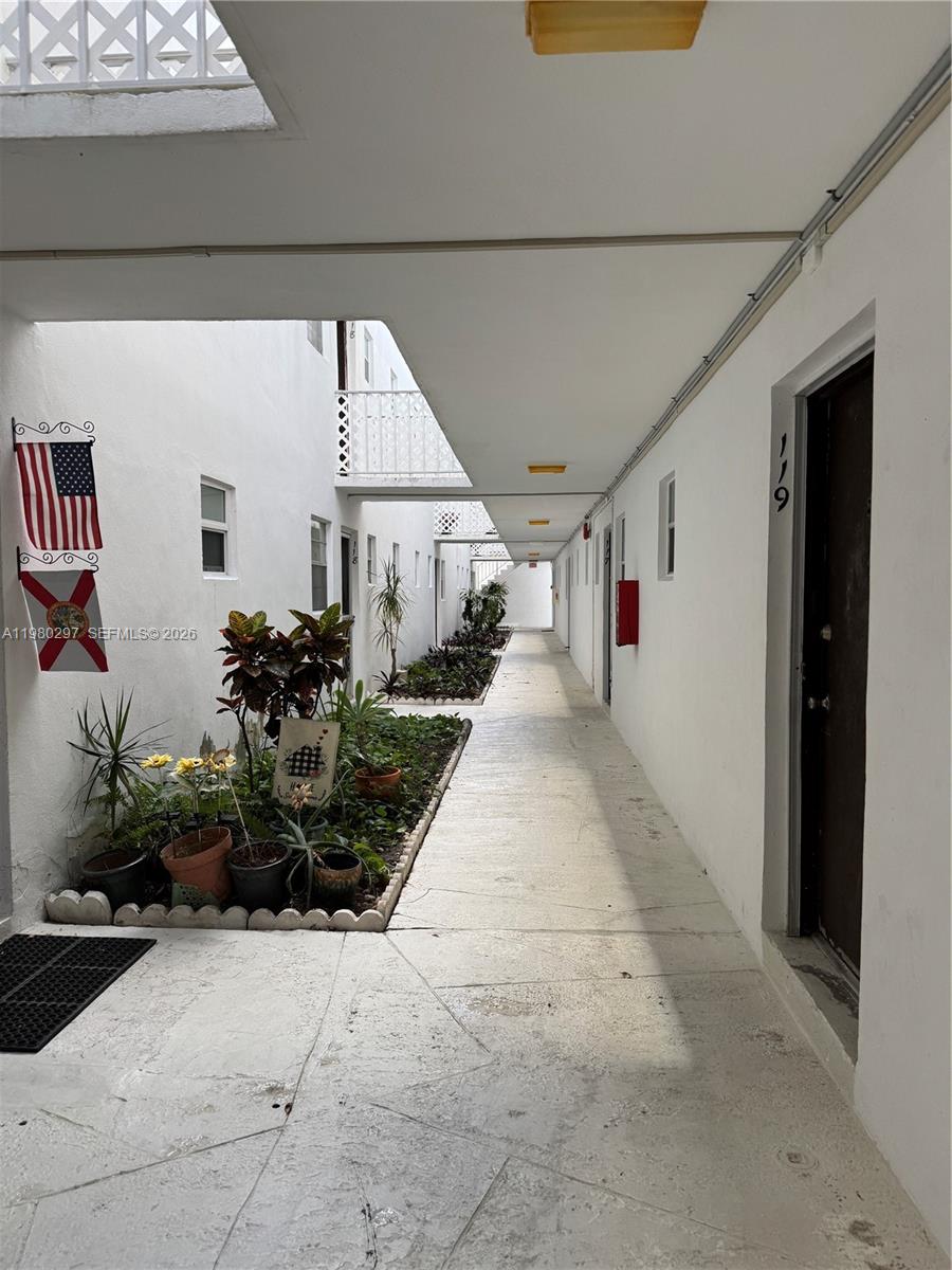 An outdoor apartment walkway features a central garden bed and doors numbered 119 — 6507 Winfield Blvd, Margate FL 33063, MARGATE, FL