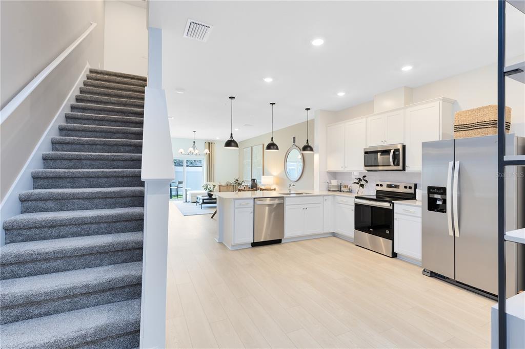 A carpeted staircase leads to an open-concept kitchen with white cabinets and stainless steel appliances — 4335 JETTY LANE NE, PALM BAY, FL