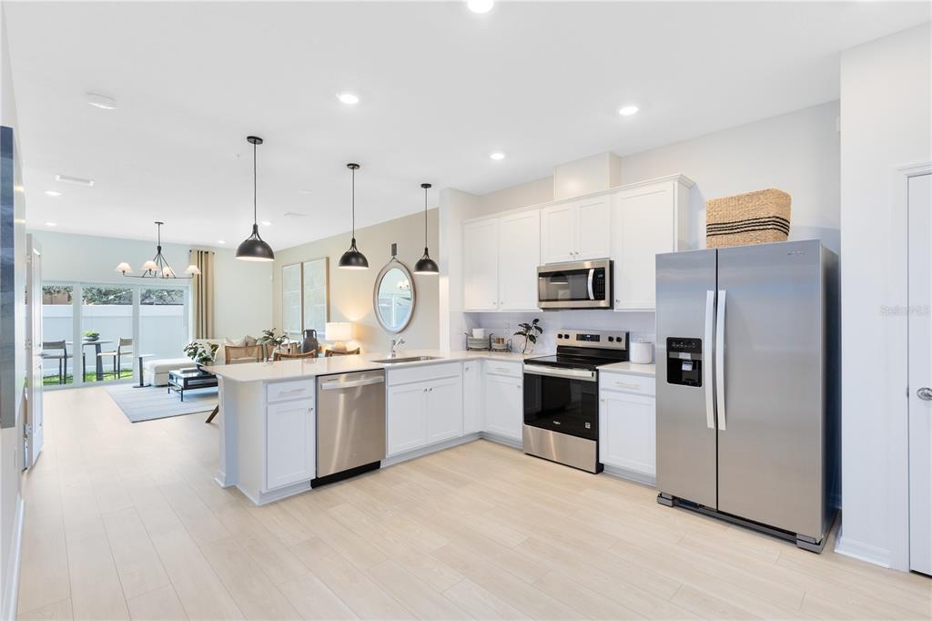 A modern kitchen with white cabinets, stainless steel appliances, and an island overlooks a living area — 4335 JETTY LANE NE, PALM BAY, FL