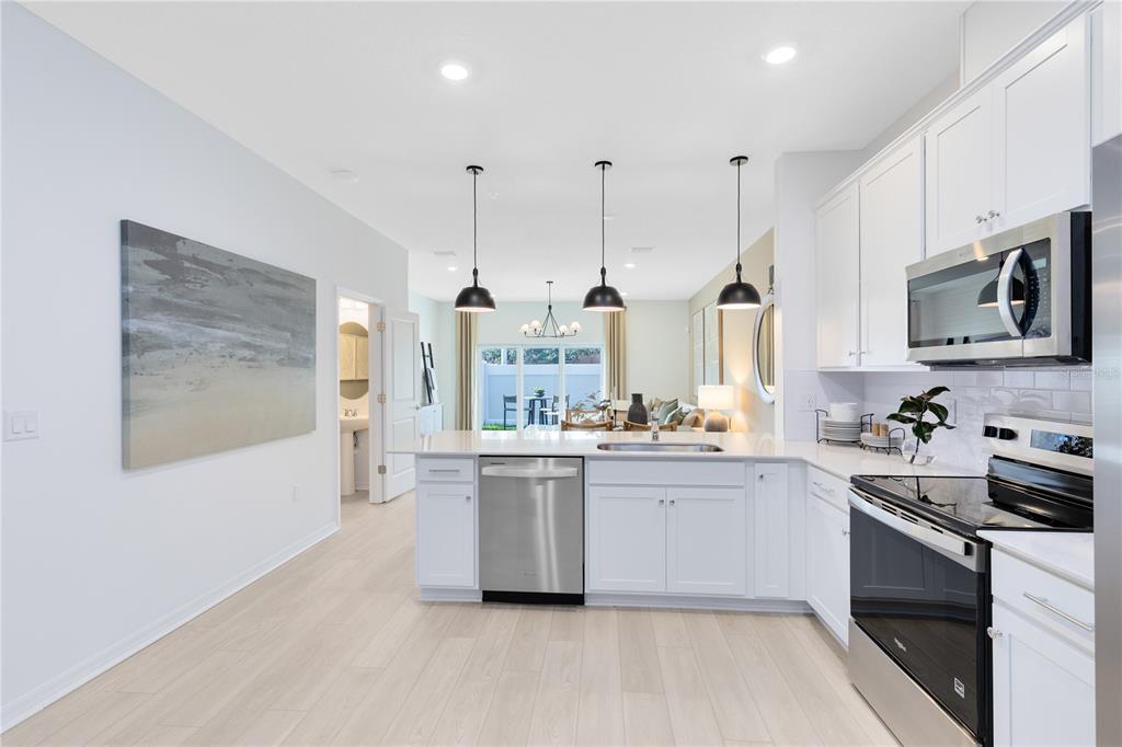A modern kitchen features white cabinets, stainless steel appliances, a quartz island, and pendant lighting — 4335 JETTY LANE NE, PALM BAY, FL