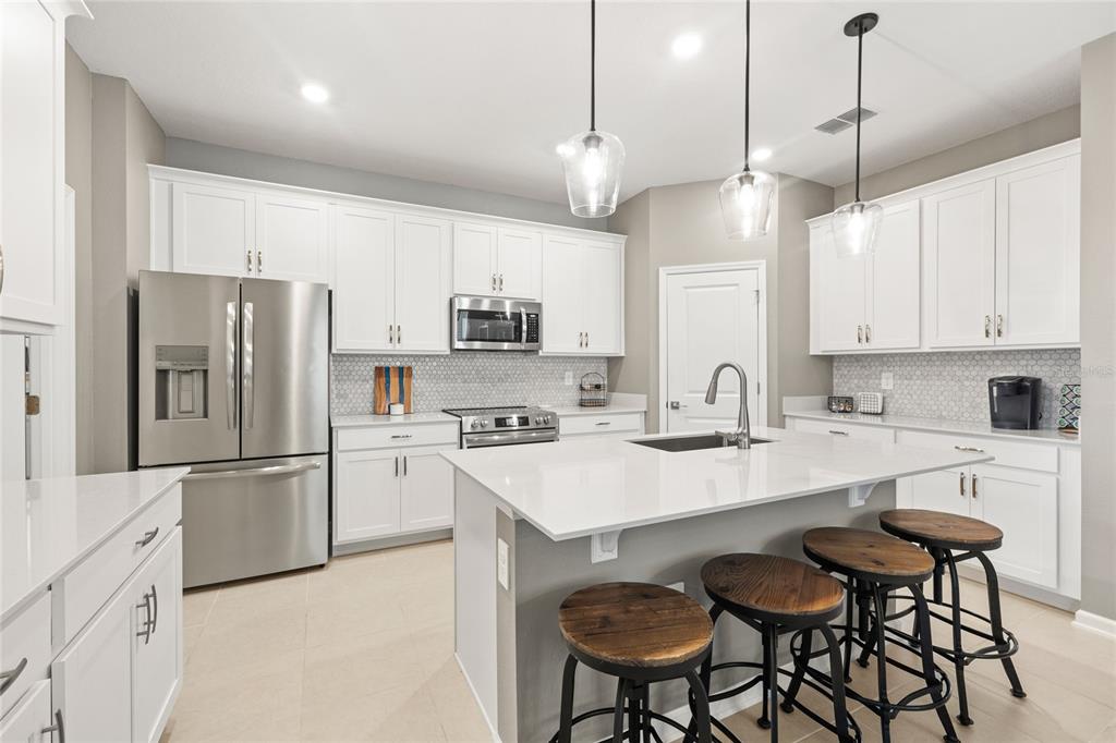 A modern kitchen features white cabinetry, stainless steel appliances, a quartz island, and bar stools — 2841 HAZE ROAD, CLERMONT, FL