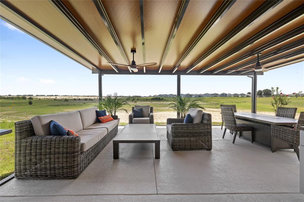 A covered outdoor patio features wicker furniture, a dining set, and views of a field — 2841 HAZE ROAD, CLERMONT, FL
