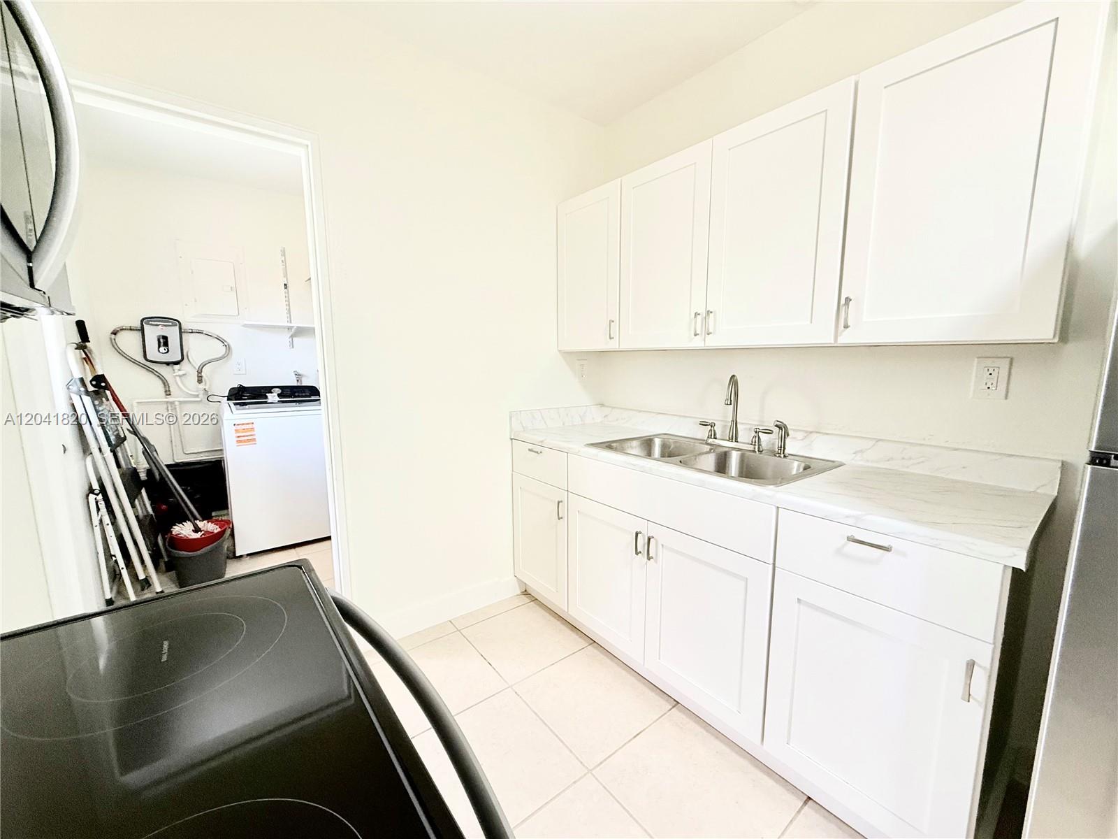 A kitchen features white cabinets, a marble-look countertop, and an adjacent laundry room — 1311 N 69th Ave, Hollywood FL 33024, HOLLYWOOD, FL