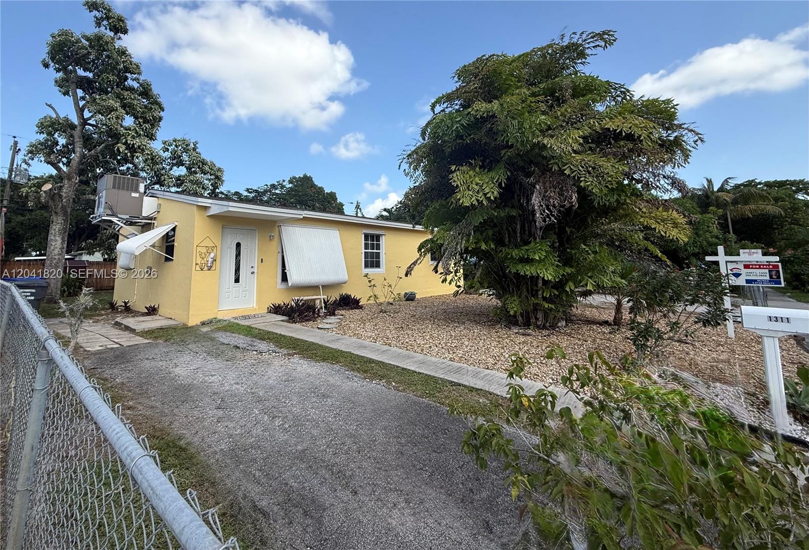 A yellow single-story house features a gravel yard, a paved driveway, and a metal fence — 1311 N 69th Ave, Hollywood FL 33024, HOLLYWOOD, FL