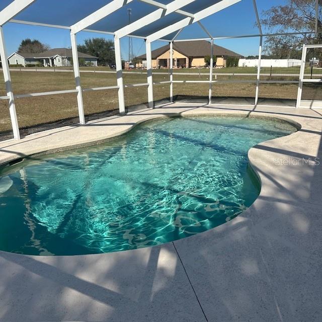 A kidney-shaped swimming pool is enclosed by a white screen cage on a concrete patio — 9300 COUNTY ROAD 128C, WILDWOOD, FL