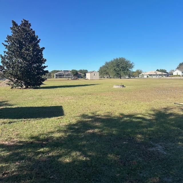 A large, grassy backyard features a mature tree, a small shed, and a fire pit — 9300 COUNTY ROAD 128C, WILDWOOD, FL