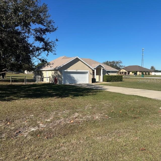 A tan single-story house with a two-car garage sits on a large, grassy lot — 9300 COUNTY ROAD 128C, WILDWOOD, FL