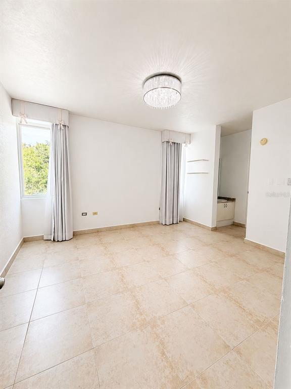 An empty bedroom features light-colored tile flooring, two windows with floor-length curtains, and a chandelier — TREASURE POINT CALLE AGUAMARINE UNIT 13, VEGA ALTA, PR