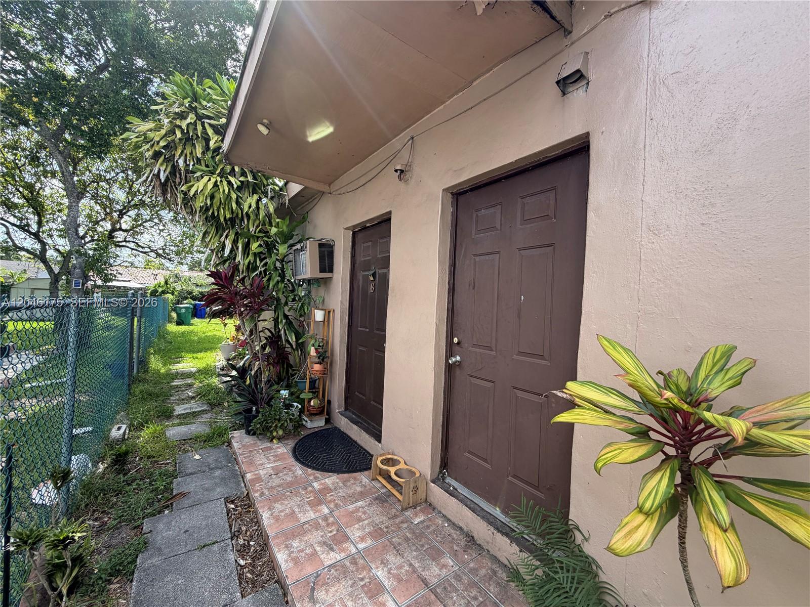 An exterior view shows two brown doors on a tiled walkway beside a chain-link fence — 745 NW 32nd Ave, Miami FL 33125, MIAMI, FL