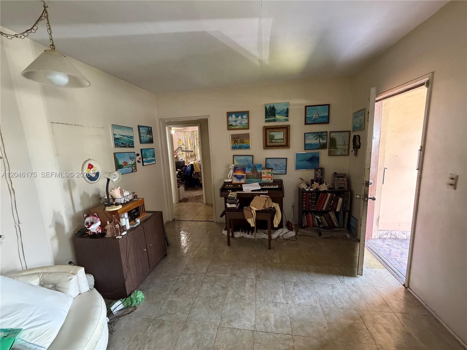 A living room features tile flooring, a piano, wall-mounted artwork, and an open doorway — 745 NW 32nd Ave, Miami FL 33125, MIAMI, FL