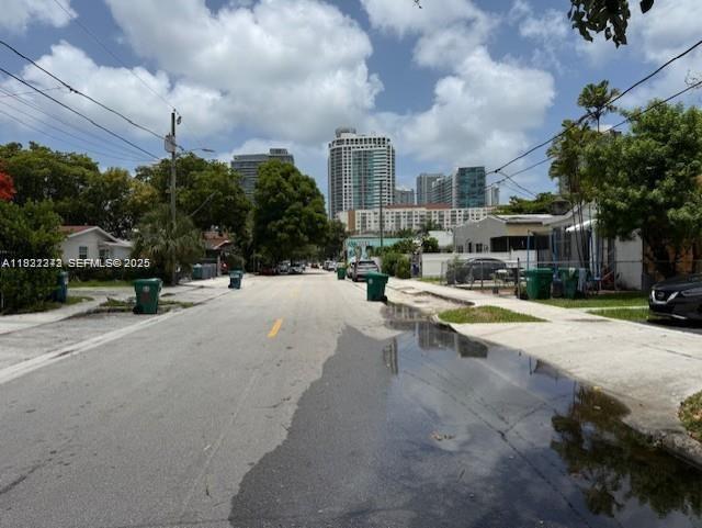 A street view shows a residential road with puddles, green trash bins, and distant high-rise buildings — 67 NW 34th St, Miami FL 33127, MIAMI, FL