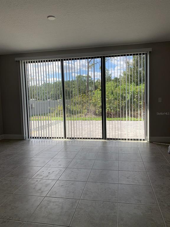 A room with large sliding glass doors, vertical blinds, and light-colored tile flooring — 4702 TERRA ESMERALDA DRIVE, KISSIMMEE, FL