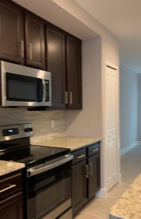 A kitchen features dark wood cabinets, stainless steel appliances, and light-colored granite countertops — 4702 TERRA ESMERALDA DRIVE, KISSIMMEE, FL