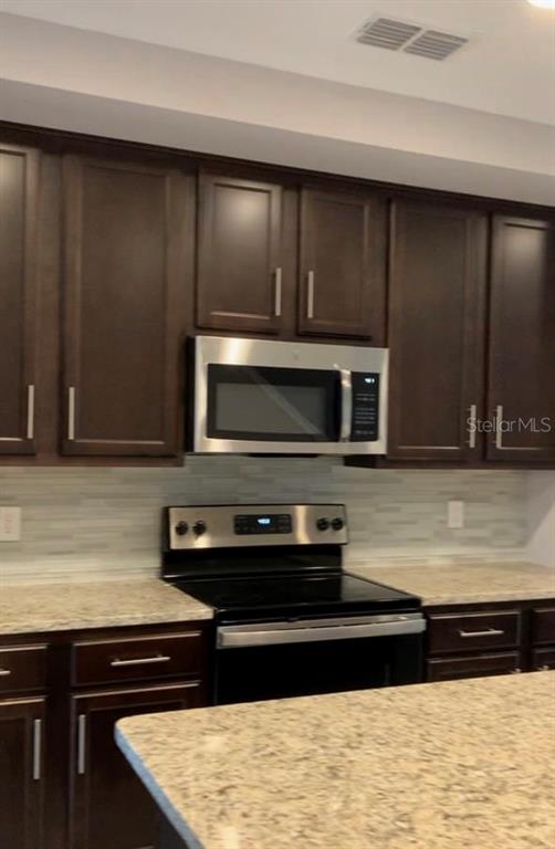 A kitchen features dark wood cabinets, stainless steel appliances, and a granite countertop island — 4702 TERRA ESMERALDA DRIVE, KISSIMMEE, FL