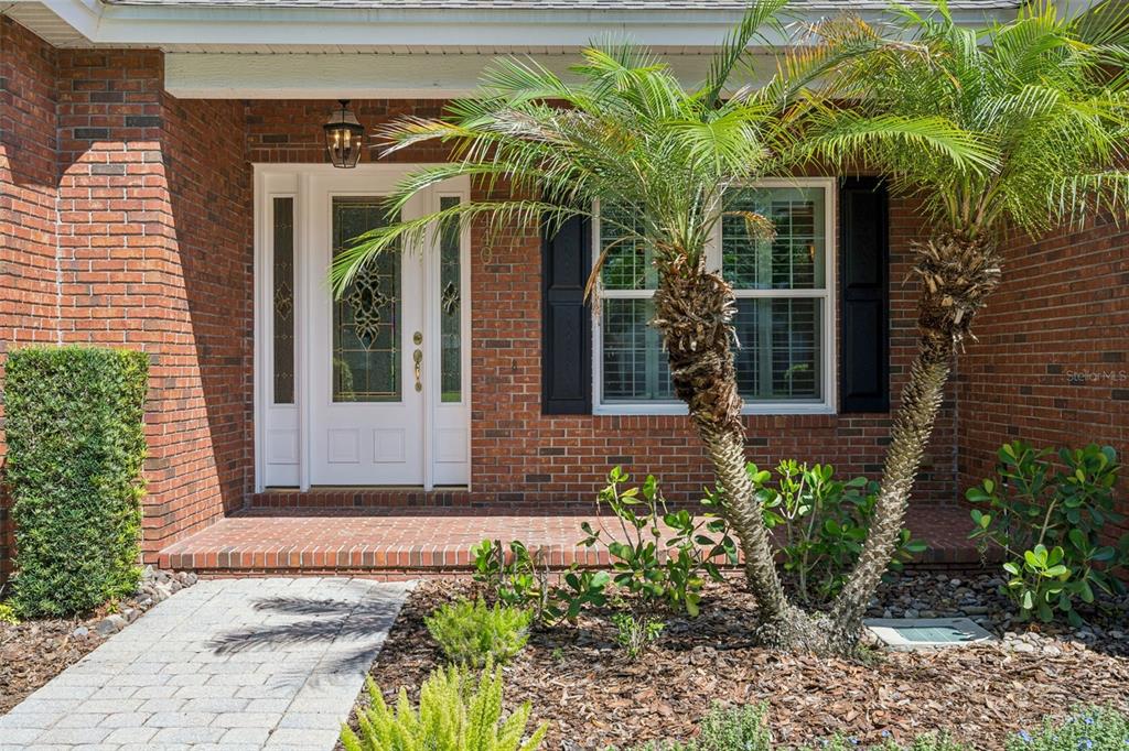 A brick house exterior features a white front door, a window with shutters, and palms — 440 TIERRA VERDE LANE, WINTER GARDEN, FL
