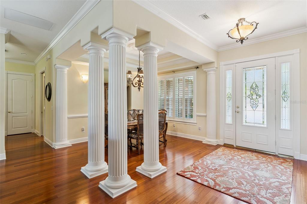 An entryway with hardwood floors, a patterned rug, and white columns framing a dining area — 440 TIERRA VERDE LANE, WINTER GARDEN, FL