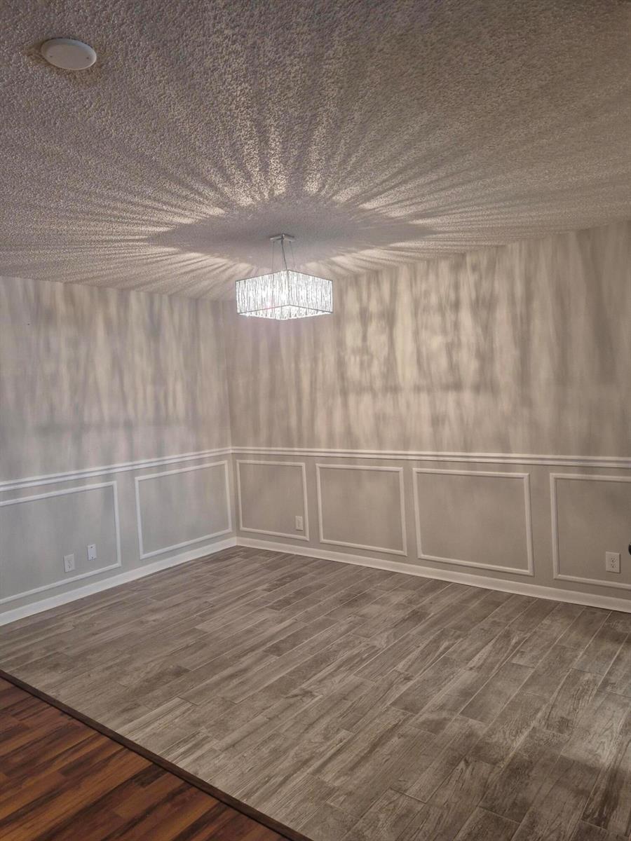 An empty room features wood-look tile flooring, three-paneled wainscoting, and a decorative crystal chandelier — 4530 NW 3rd Street # B, Delray Beach FL 33445, DELRAY BEACH, FL