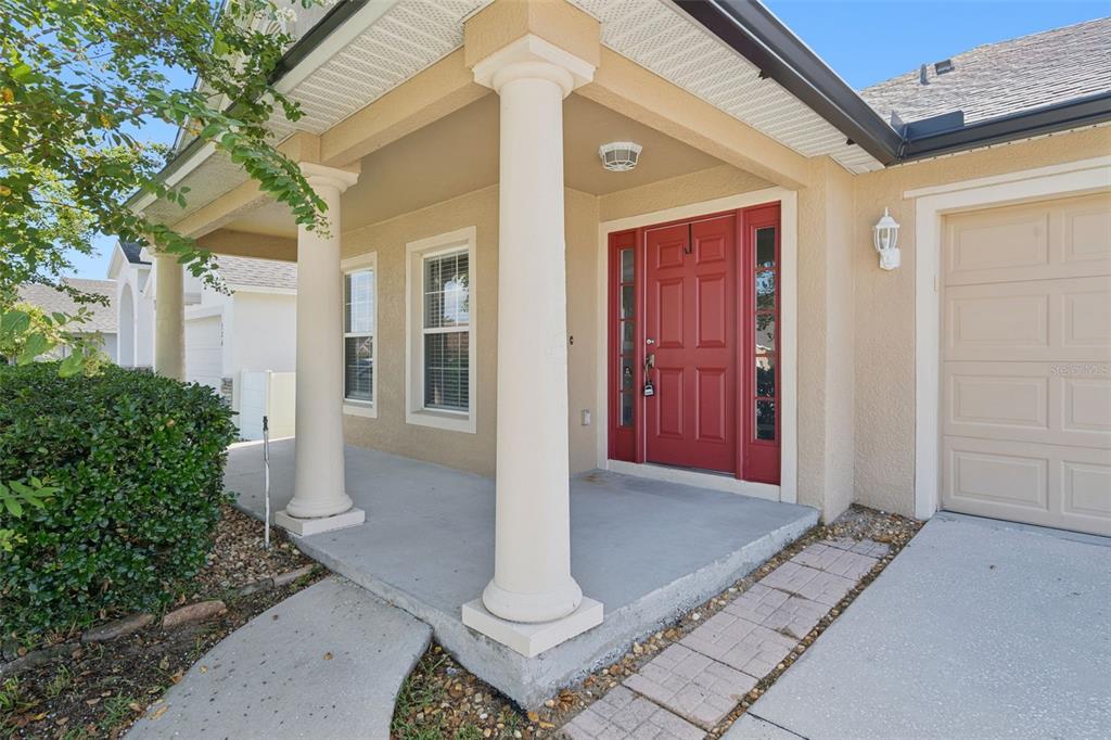 A tan house exterior features a covered porch with white columns and a red door — 324 RED KITE DRIVE, GROVELAND, FL