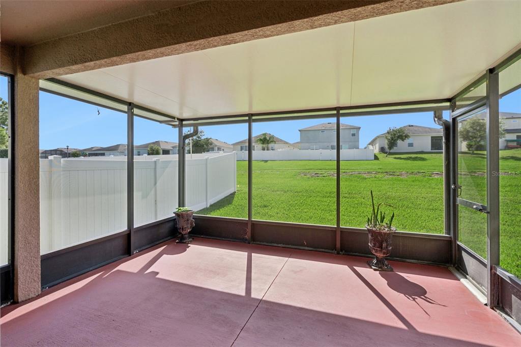 A screened-in patio with a red concrete floor overlooks a grassy backyard and white fence — 324 RED KITE DRIVE, GROVELAND, FL