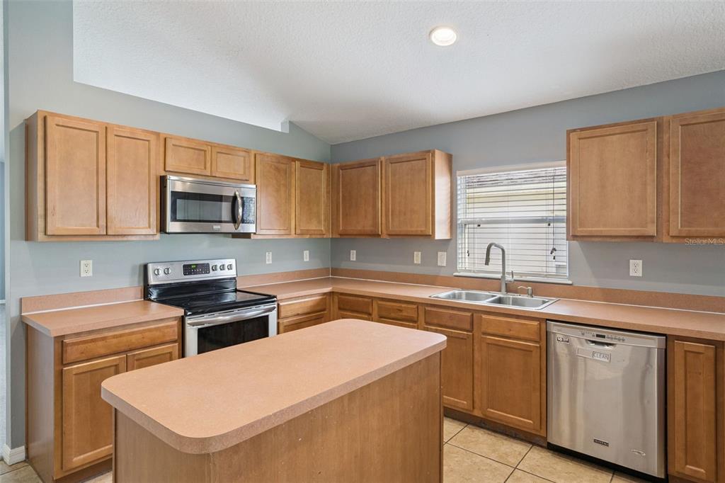 A kitchen features wood cabinets, laminate countertops, stainless steel appliances, and a central island — 324 RED KITE DRIVE, GROVELAND, FL