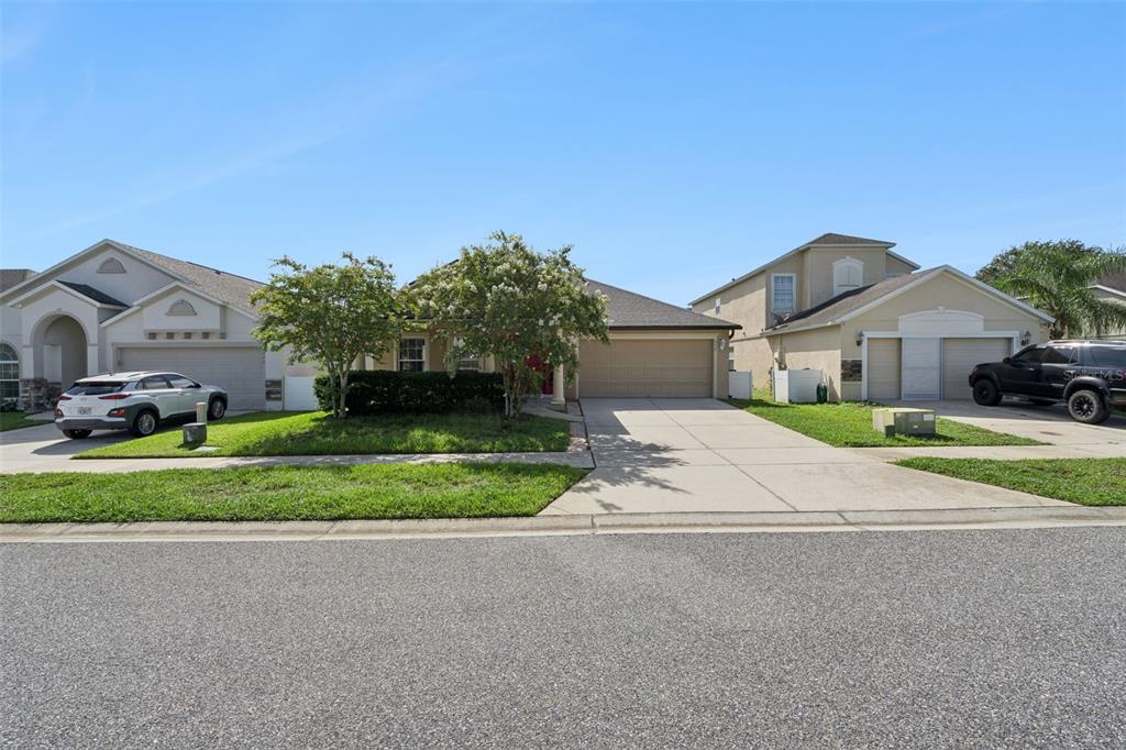 A single-story suburban house with a tan exterior, a two-car garage, and two small trees — 324 RED KITE DRIVE, GROVELAND, FL