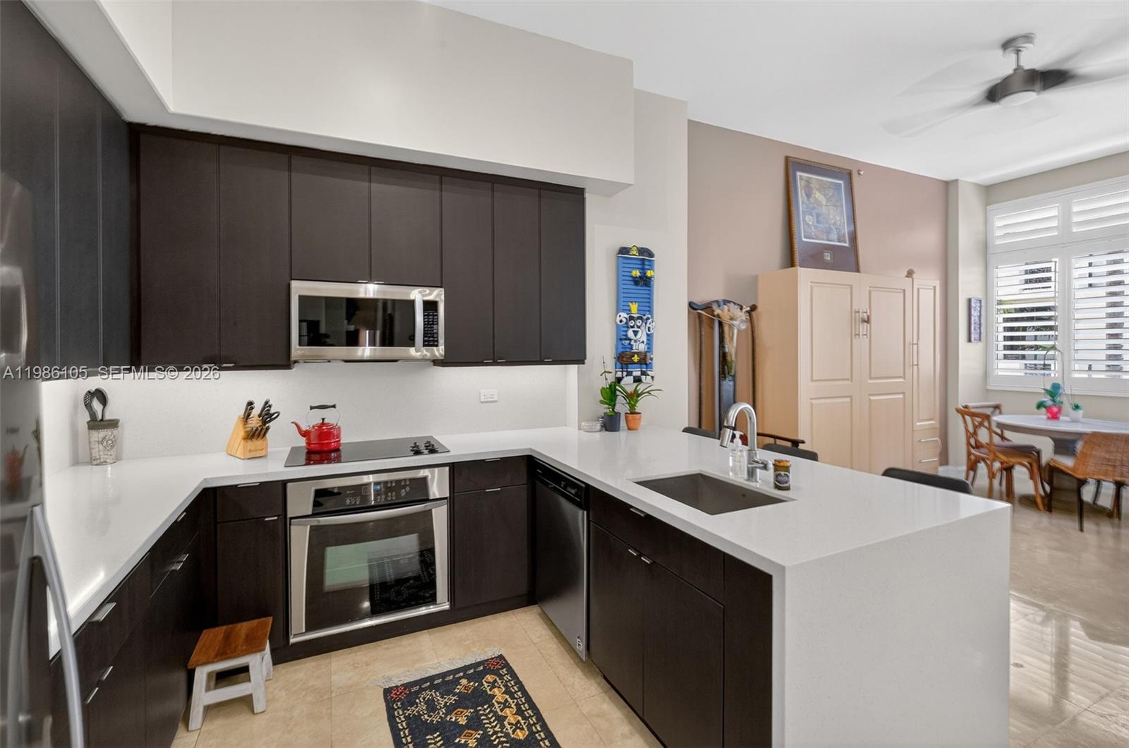 A modern kitchen features dark cabinetry, white countertops, stainless steel appliances, and an island sink — 1805 Ponce De Leon Blvd # 616, Coral Gables FL 33134, CORAL GABLES, FL