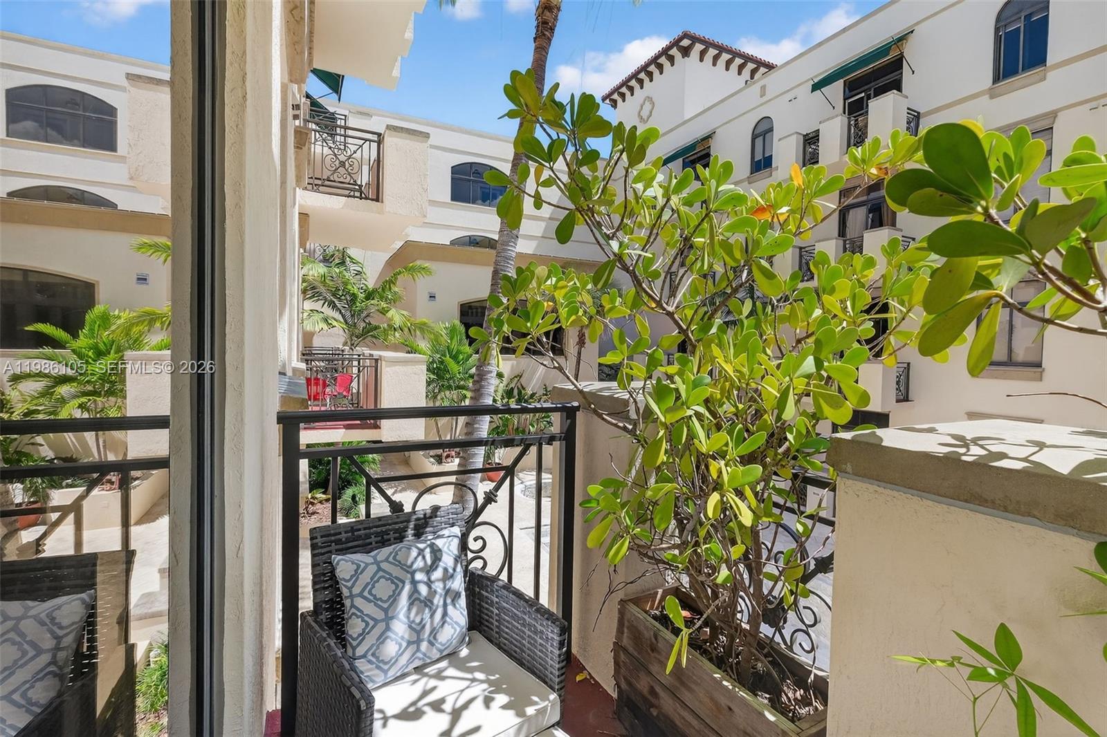 A balcony with a wicker chair and a potted plant overlooks a courtyard building complex — 1805 Ponce De Leon Blvd # 616, Coral Gables FL 33134, CORAL GABLES, FL