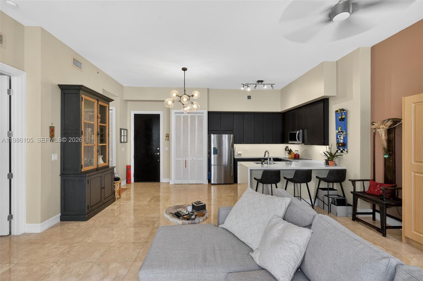 This open-concept living area features a kitchen with dark cabinetry, tile flooring, and a sofa — 1805 Ponce De Leon Blvd # 616, Coral Gables FL 33134, CORAL GABLES, FL