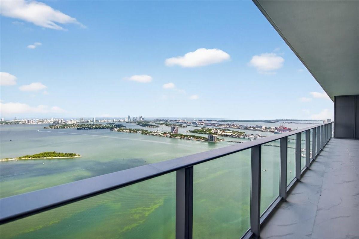 A high-rise balcony with a glass railing overlooks a bay with islands and a city skyline — 700 NE 24th Street # 5202, Miami FL 33137, MIAMI, FL