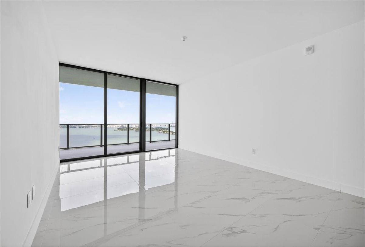 An empty room with white walls, white marble-look tile floors, and floor-to-ceiling windows overlooking water — 700 NE 24th Street # 5202, Miami FL 33137, MIAMI, FL