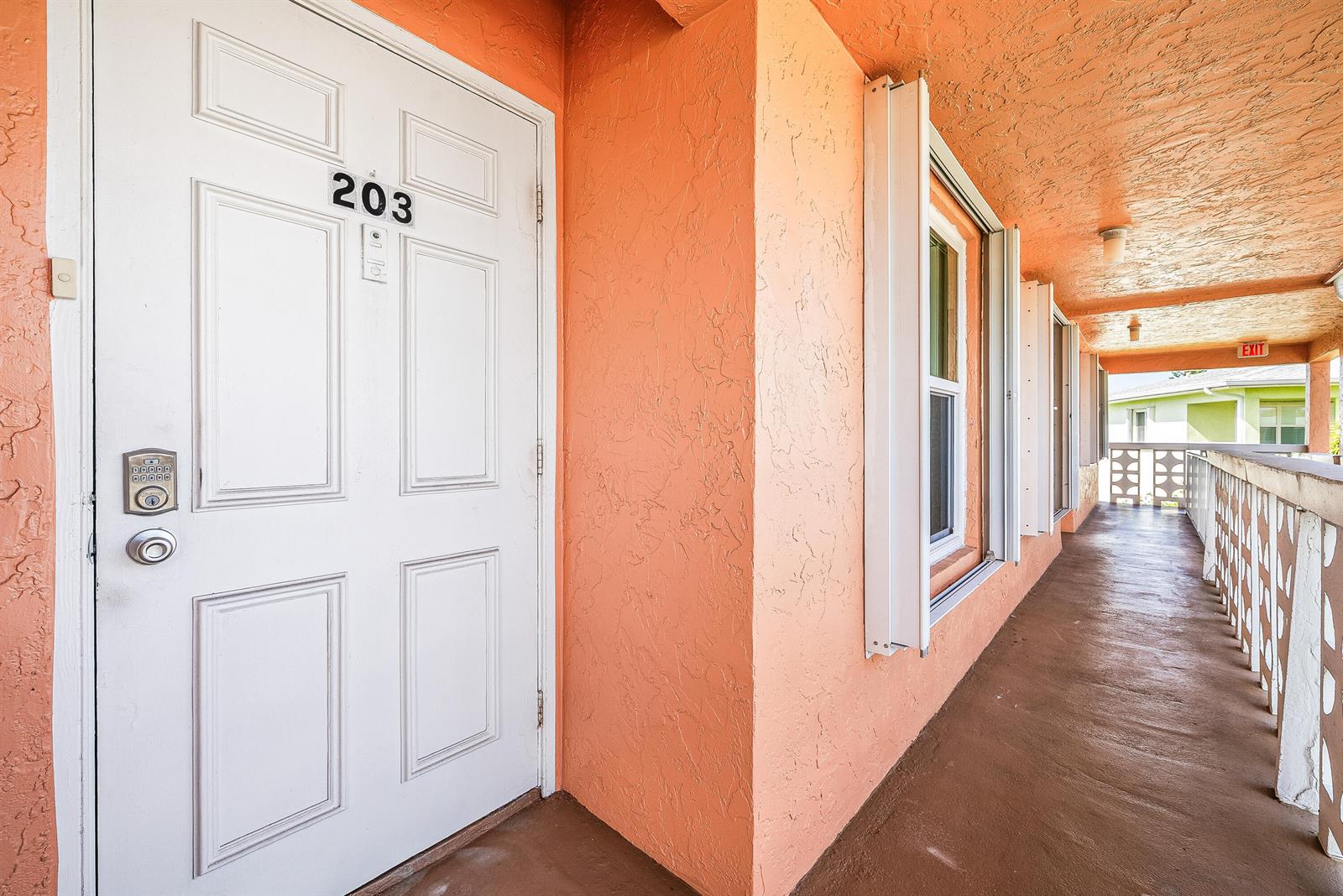 An exterior walkway features a white door labeled 203, peach-colored stucco walls, and white railings — 1640 NW 19TH Terrace # 203, Delray Beach FL 33445, DELRAY BEACH, FL