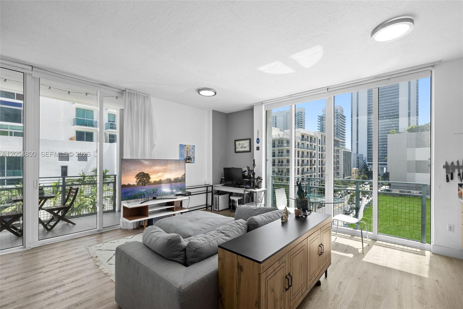 A living room features a gray sofa, a television, a desk, and floor-to-ceiling windows — 350 NE 24th St # 401, Miami FL 33137, MIAMI, FL