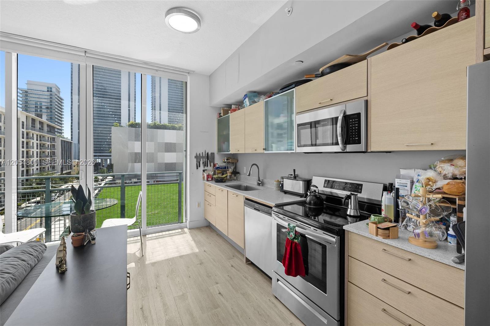 A modern kitchen features light wood cabinetry, stainless steel appliances, and a balcony with city views — 350 NE 24th St # 401, Miami FL 33137, MIAMI, FL